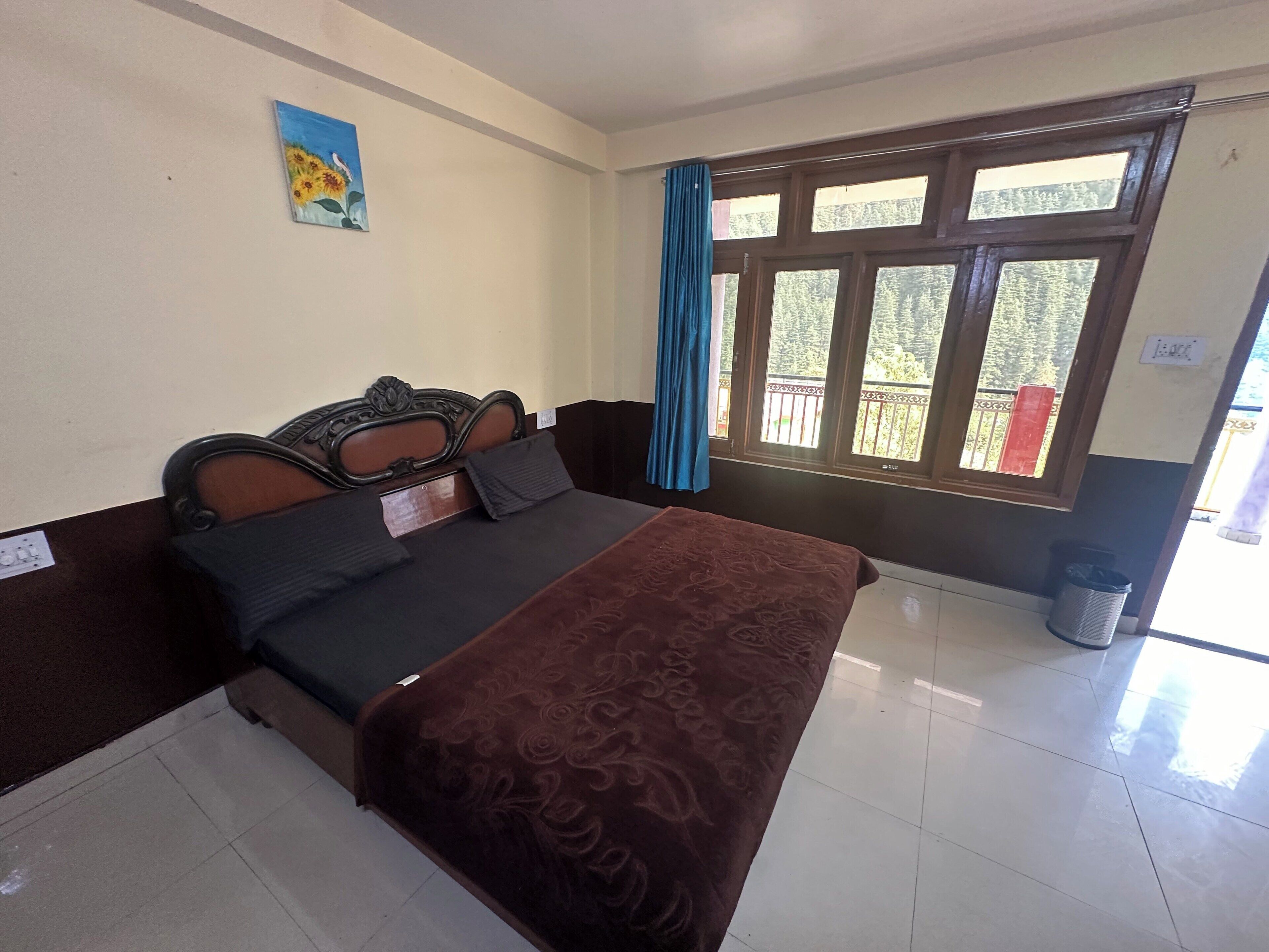 A bedroom with a bed, a painting, a window with curtains, and a balcony view.