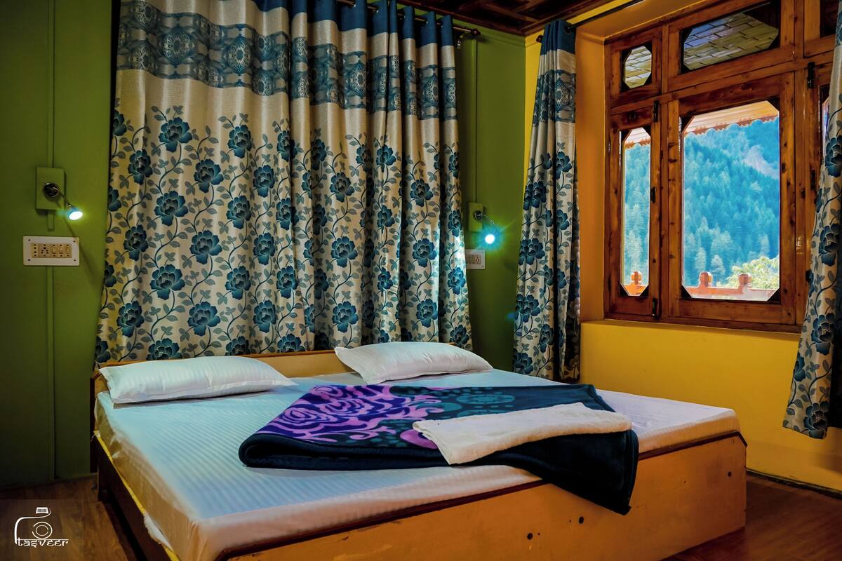 A room with a bed, floral curtains, a window with a view, and a wall socket.