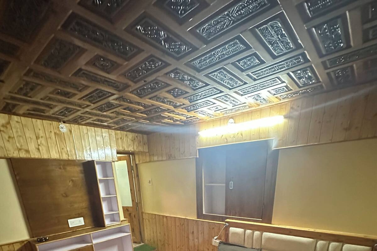 A bedroom with a wooden ceiling, a bed with a patterned blanket, a nightstand, a wardrobe, and a mirror.