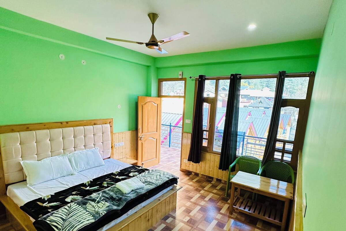A room with a bed, a wooden cabinet, a window with curtains, and a view of buildings outside.