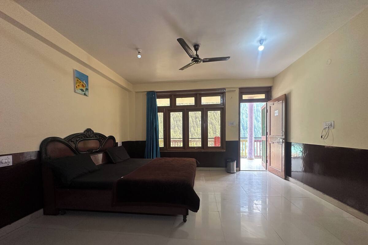A hotel room with a bed, a ceiling fan, a window with curtains, and a door leading outside.