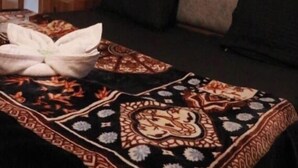 A wooden-paneled room with a bed, a sofa, and a patterned bedspread. - Pirates Of Parvati (Bhuntar)