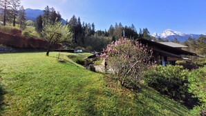 A cabin with a sloped roof, surrounded by a well-maintained lawn and flowering trees. - Vacation apartment 6 for max. 4 persons (Berchtesgaden)