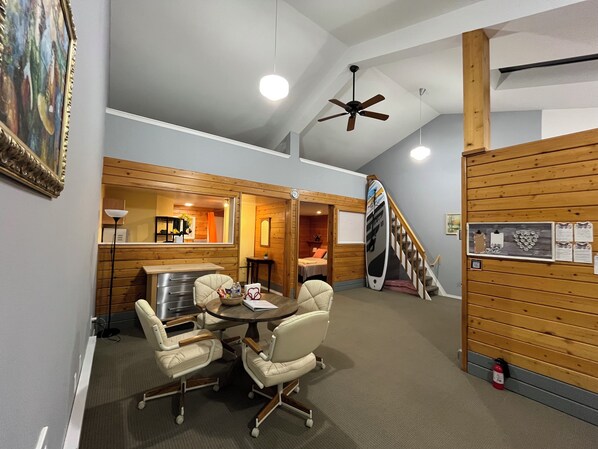 A room with a dining table and chairs, a ceiling fan, a wooden staircase, and a surfboard leaning against the wall. - Whispering Pines Farmhouse (Redmond)