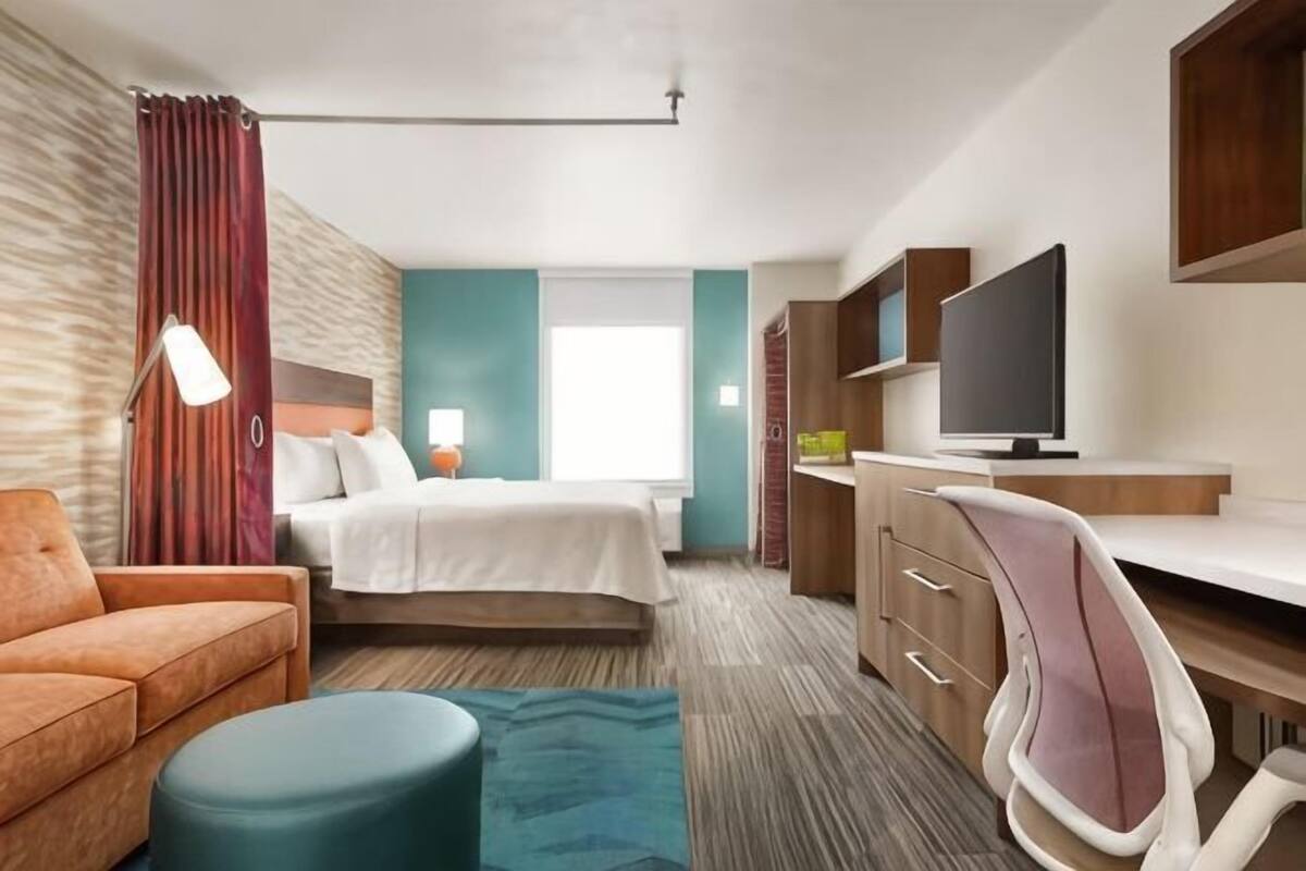 A hotel room with a bed, a desk, a TV, a chair, and a sofa.