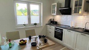 A modern kitchen with white cabinets, a black range hood, and a window with blinds.