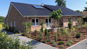 A two-story house with a sloped roof, solar panels, and a landscaped garden with various plants and a wooden deck.