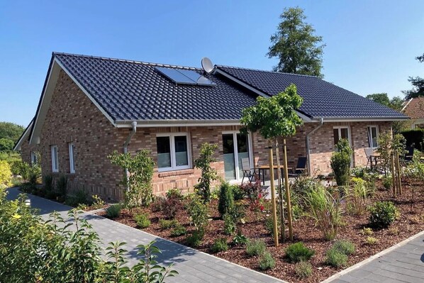 A two-story house with a sloped roof, solar panels, and a landscaped garden with various plants and a wooden deck.