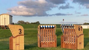 Three wicker chairs with striped canopies, numbered 3, 4, and 5, in a grassy field.
