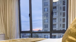 A hotel room with a large window, a bed with white bedding, and a view of a cityscape. - Alba Garden (Nairobi)