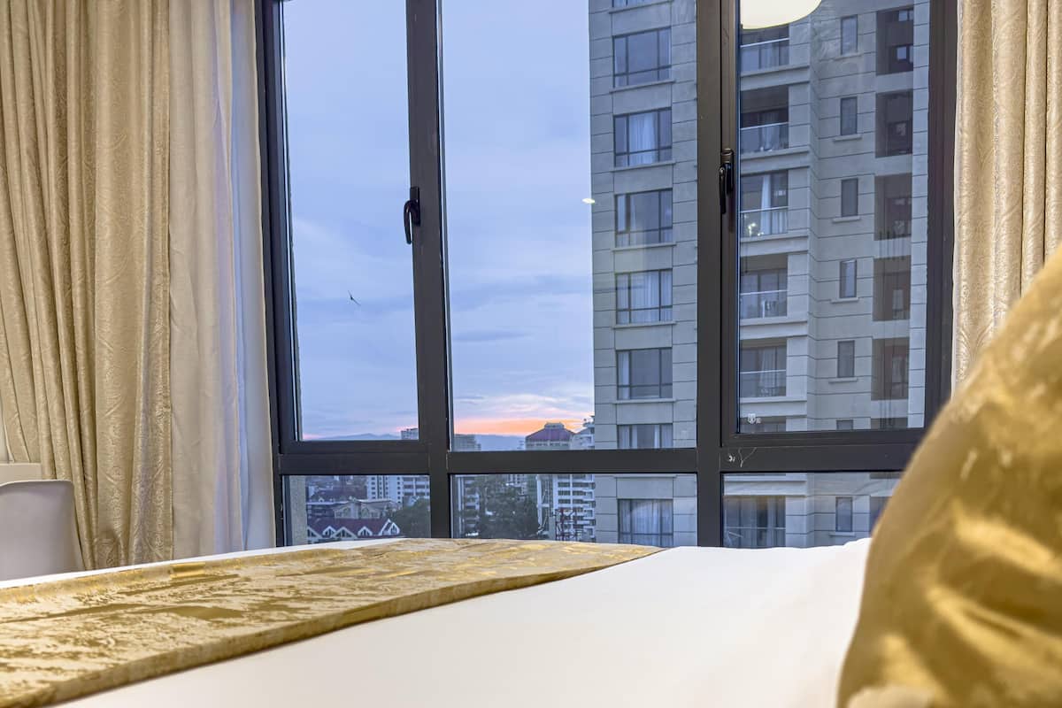 A hotel room with a large window, a bed with white bedding, and a view of a cityscape.