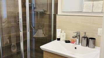 Un bagno moderno con doccia vetrata, lavandino bianco e accessori per la cura personale, e un portasciugamani.
