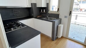 Een moderne keuken met een gasfornuis, zwarte aanrechtbladen, witte kasten, een raam en een radiator.