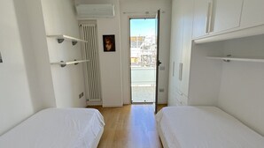 Een kamer met twee bedden, een radiator, een deur naar buiten en een witte muur met een afbeelding.