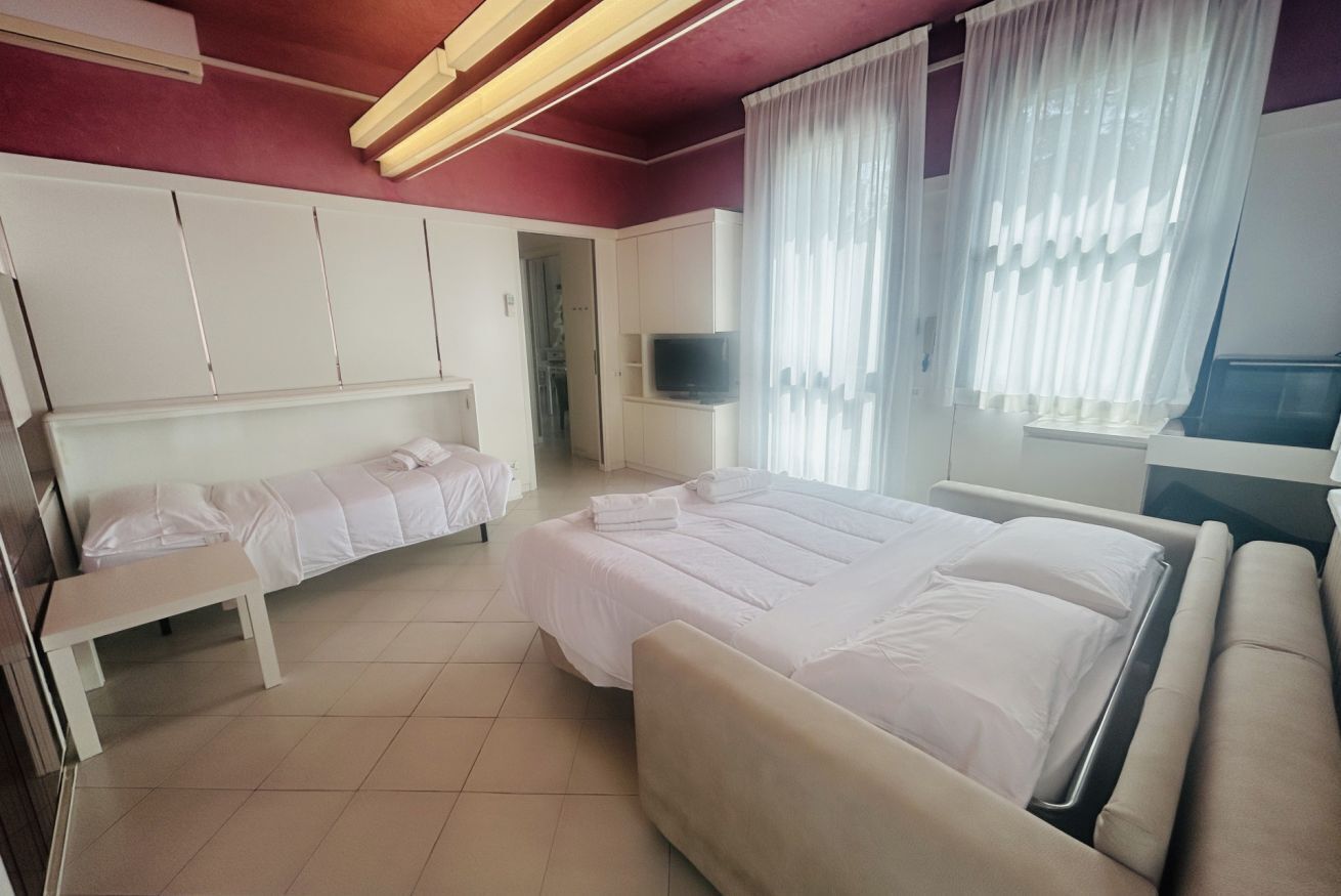 A hotel room with a large bed, a smaller bed, a bench, a TV, and a wardrobe.