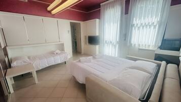 A hotel room with a large bed, a smaller bed, a bench, a TV, and a wardrobe.