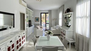 A modern living room with a dining area, white furniture, and a large window with curtains. - Villa Trieste Flexrent - Abyssinia (Riccione)