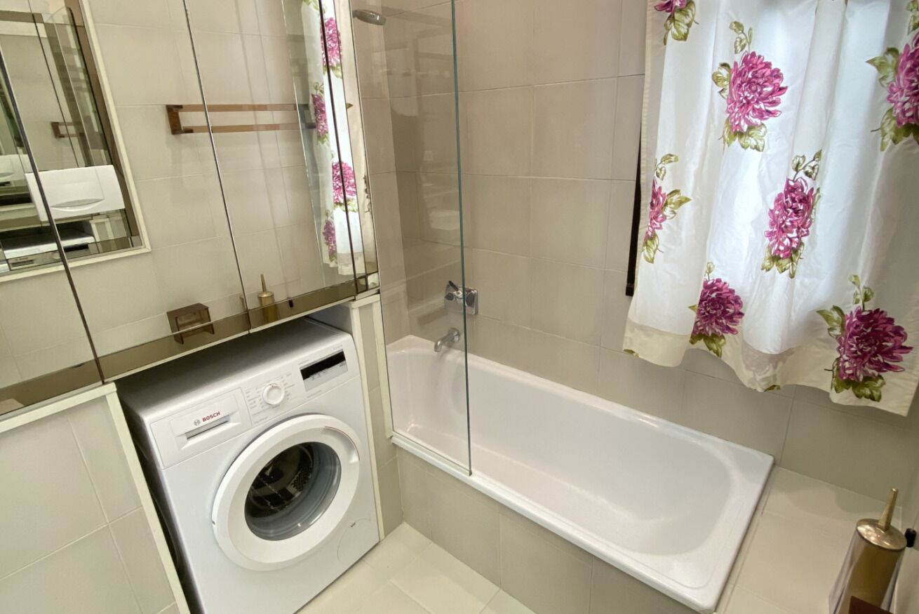 Un baño con lavadora Bosch, ducha envuelta en vidrio y bañera.