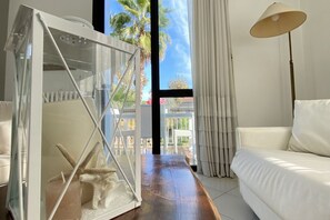 A modern living room with a white sofa, a glass table with a starfish decoration, and a view of palm trees through large windows. - Villa Trieste Flexrent - Abyssinia   (Riccione)