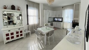 A modern kitchen with white cabinets, a dining table with chairs, and a TV. - Villa Trieste Flexrent - Abyssinia (Riccione)