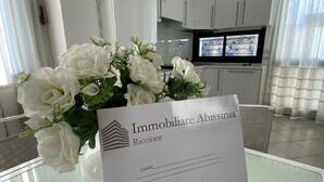 A reception area with a white flower arrangement, a sign reading "Immobiliare Abissinia Riccione," and a modern kitchen in the background. - Villa Trieste Flexrent - Abyssinia (Riccione)