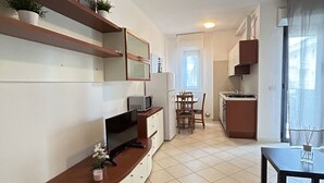Une cuisine compacte avec un coin repas, un téléviseur posé sur un meuble en bois et une petite table avec une bougie.