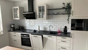 A modern kitchen with white cabinetry, a black range hood, a built-in oven, a sink, and a countertop with various appliances.
