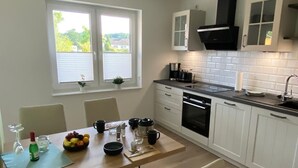 A modern kitchen with white cabinets, a black range hood, and a window with blinds.