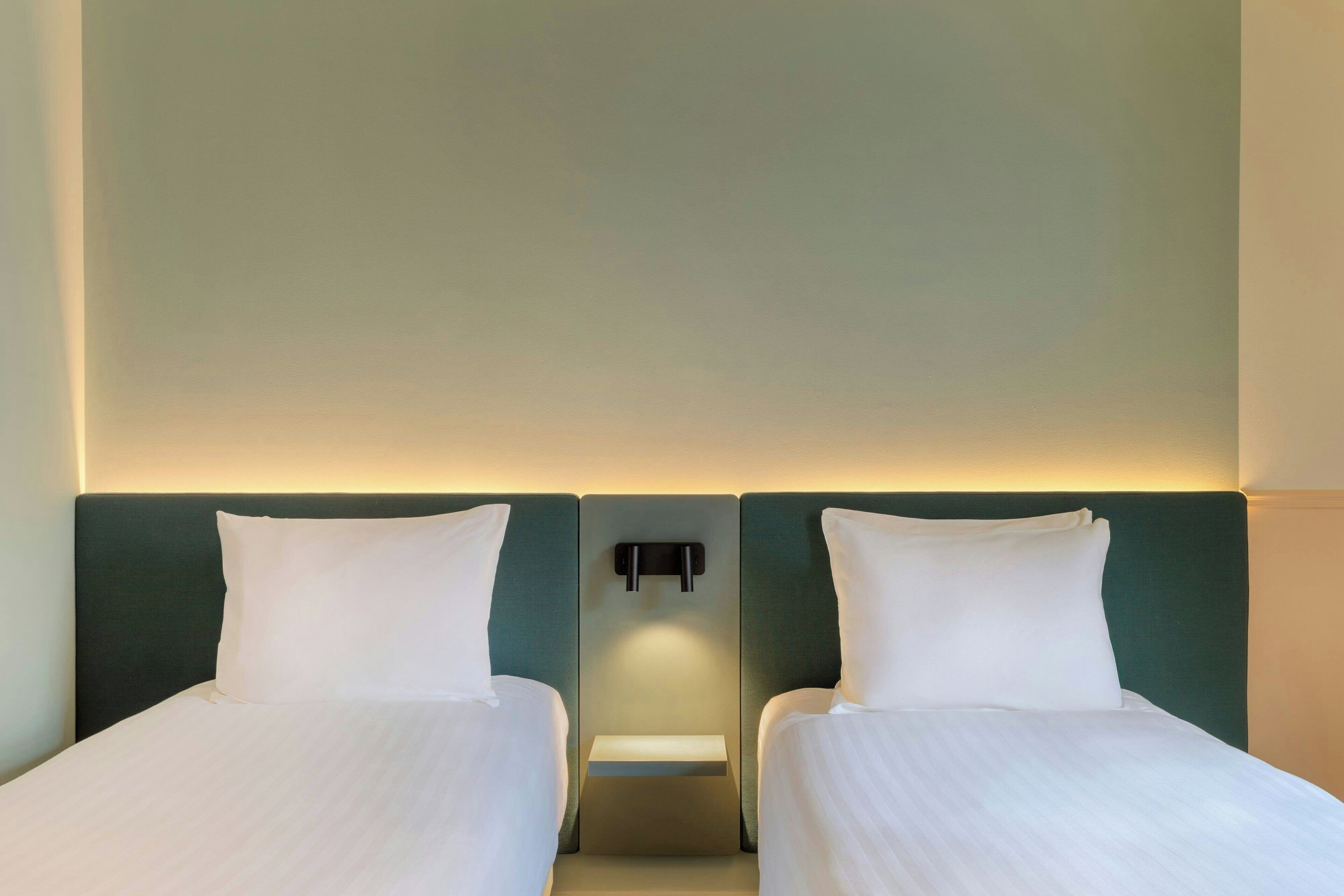 A hotel room with two single beds, a bedside table, and a wall-mounted light fixture.