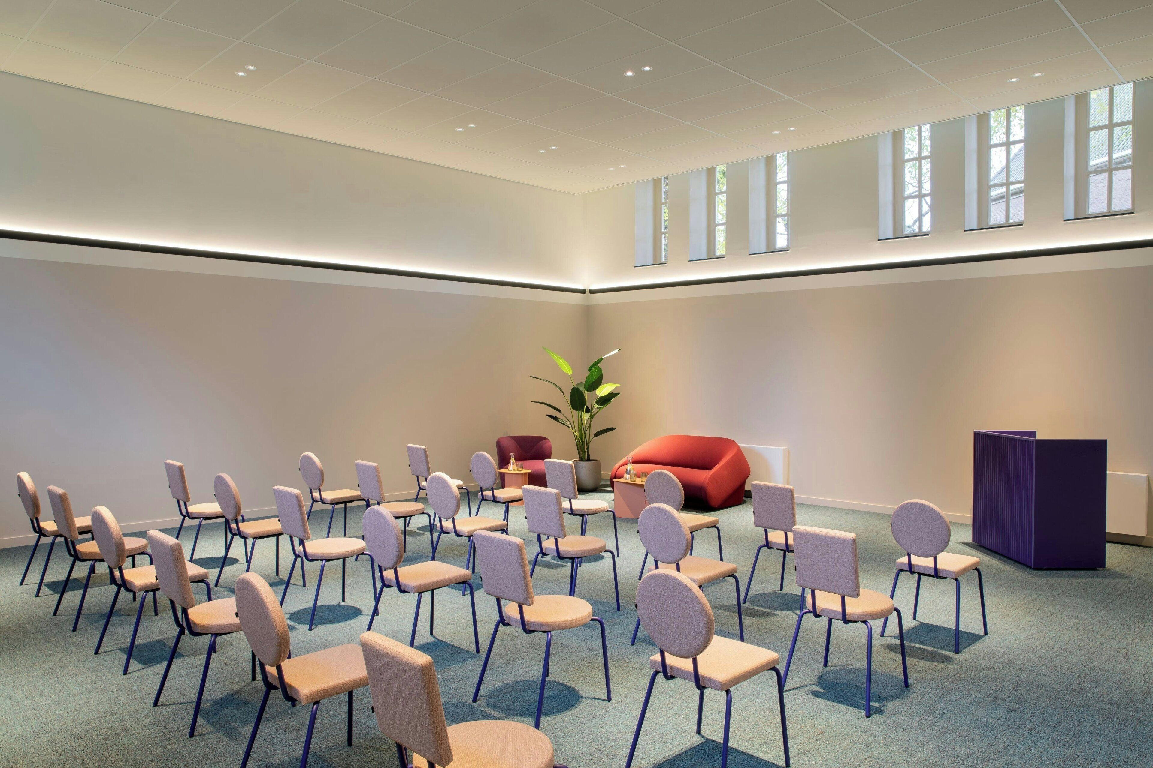 A conference room with rows of chairs, a red sofa, a potted plant, and a purple podium.