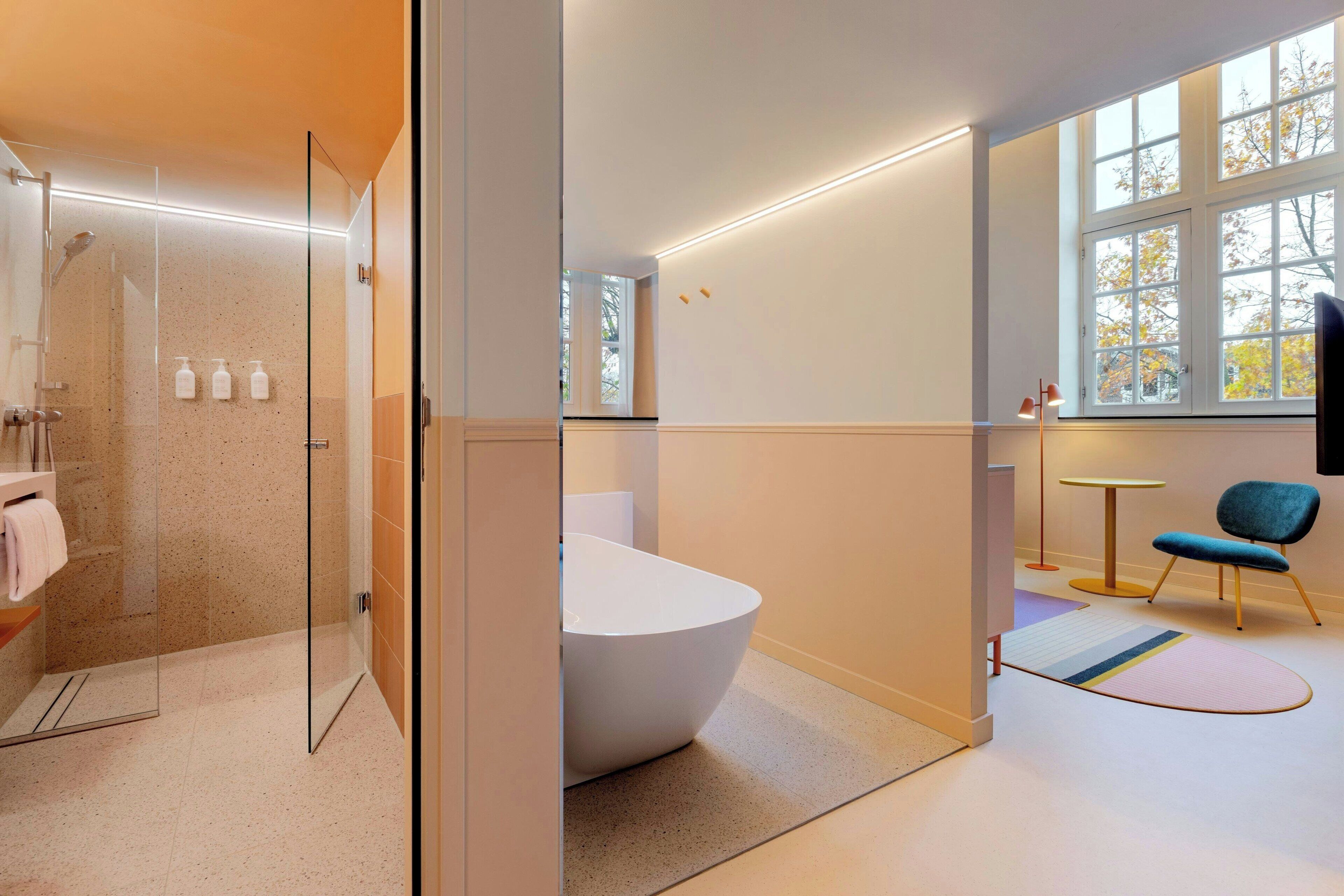 A modern bathroom with a glass-enclosed shower, a freestanding bathtub, and a window with autumn foliage.