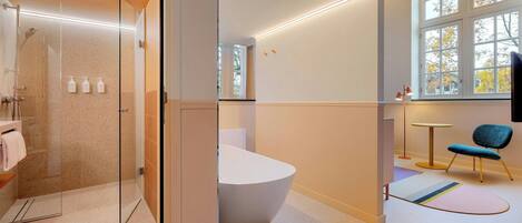 A modern bathroom with a glass-enclosed shower, a freestanding bathtub, and a window with autumn foliage.