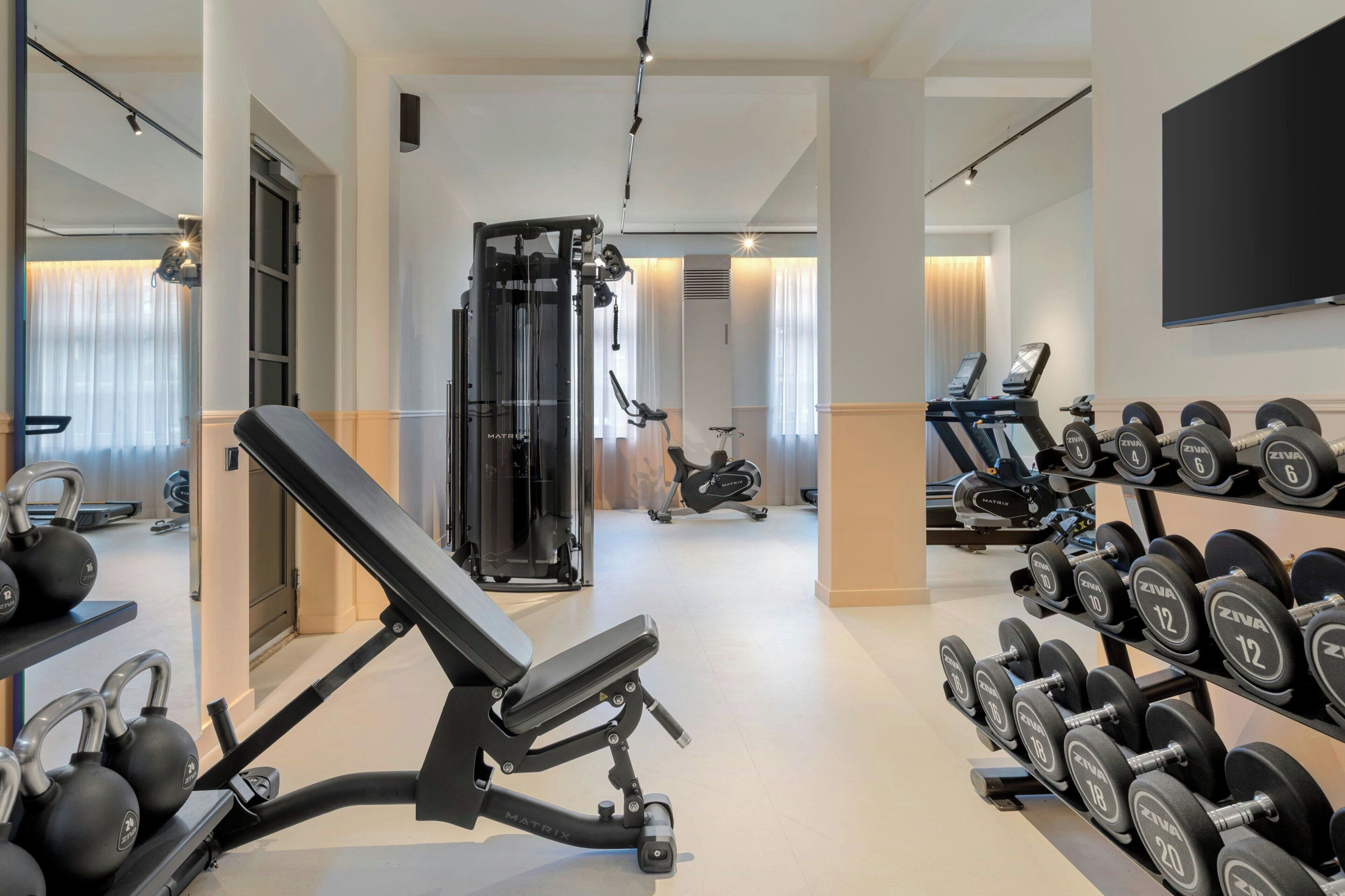 Un gimnasio con banca para press de pesas, mancuernas, máquina de poleas y equipo cardiovascular.