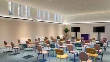 A conference room with rows of colorful chairs, a large window, and two black screens on the wall.