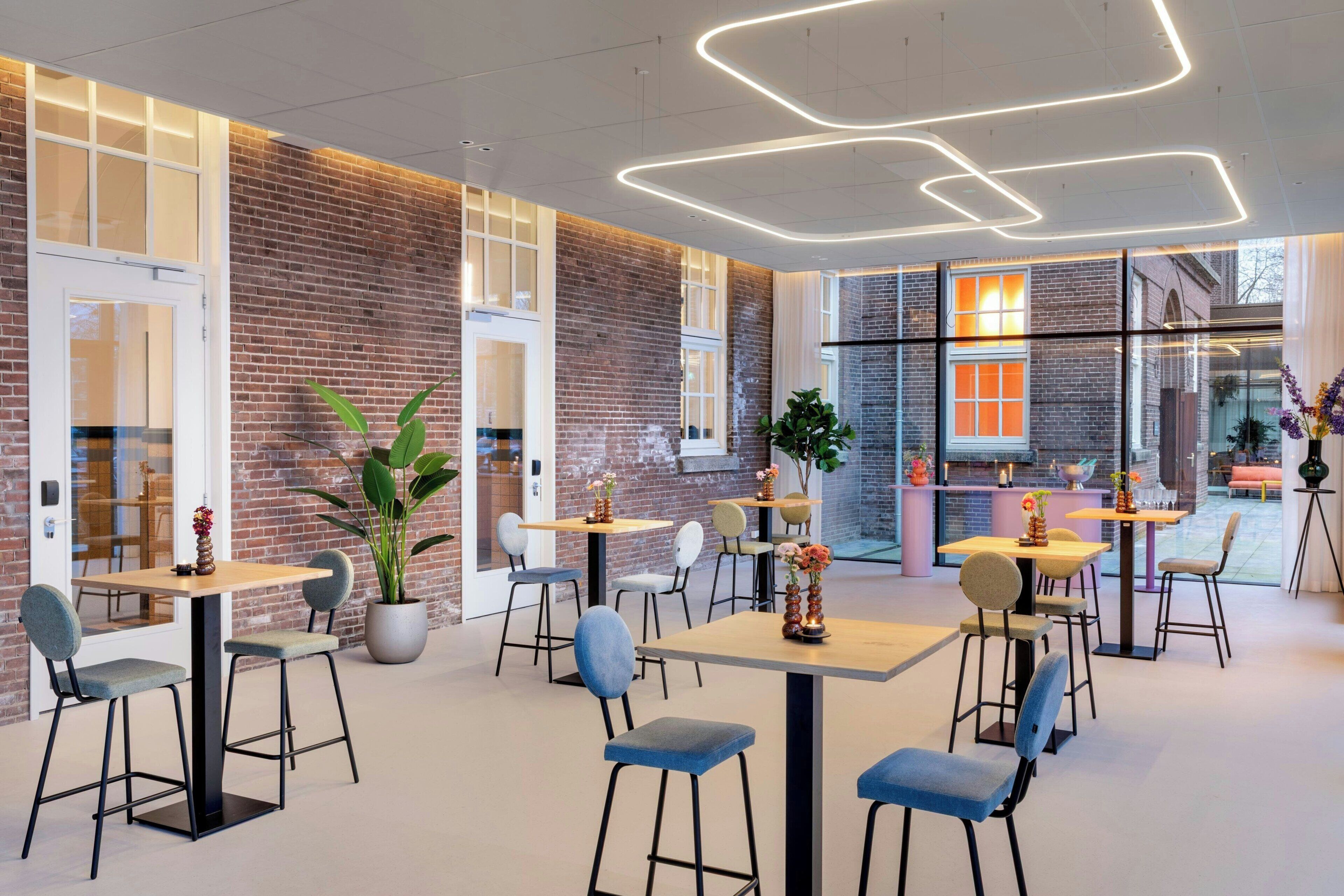 A modern interior with brick walls, large windows, and a mix of seating arrangements including tables and chairs.