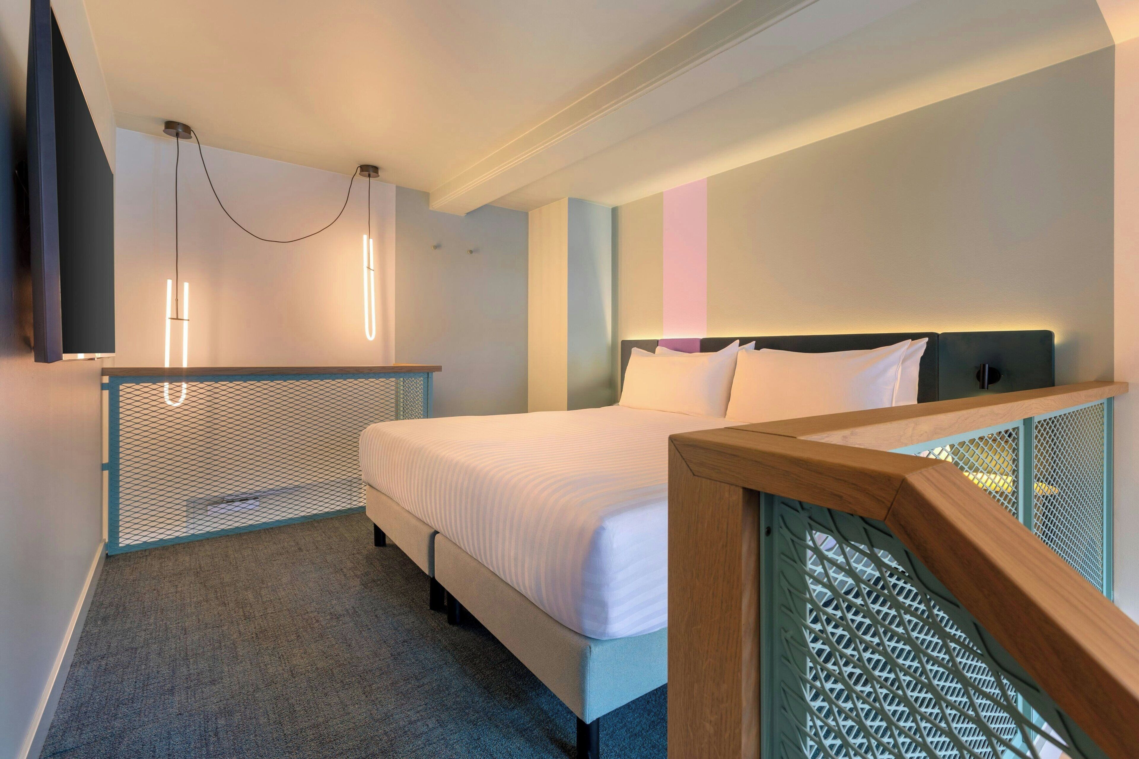 Habitación de hotel moderna con una cama grande, un televisor montado en la pared y un balcón con barandilla.