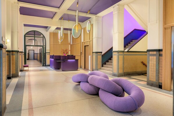 Un hall d’entrée avec un comptoir de réception, un escalier et un espace détente unique, aux couleurs violettes.