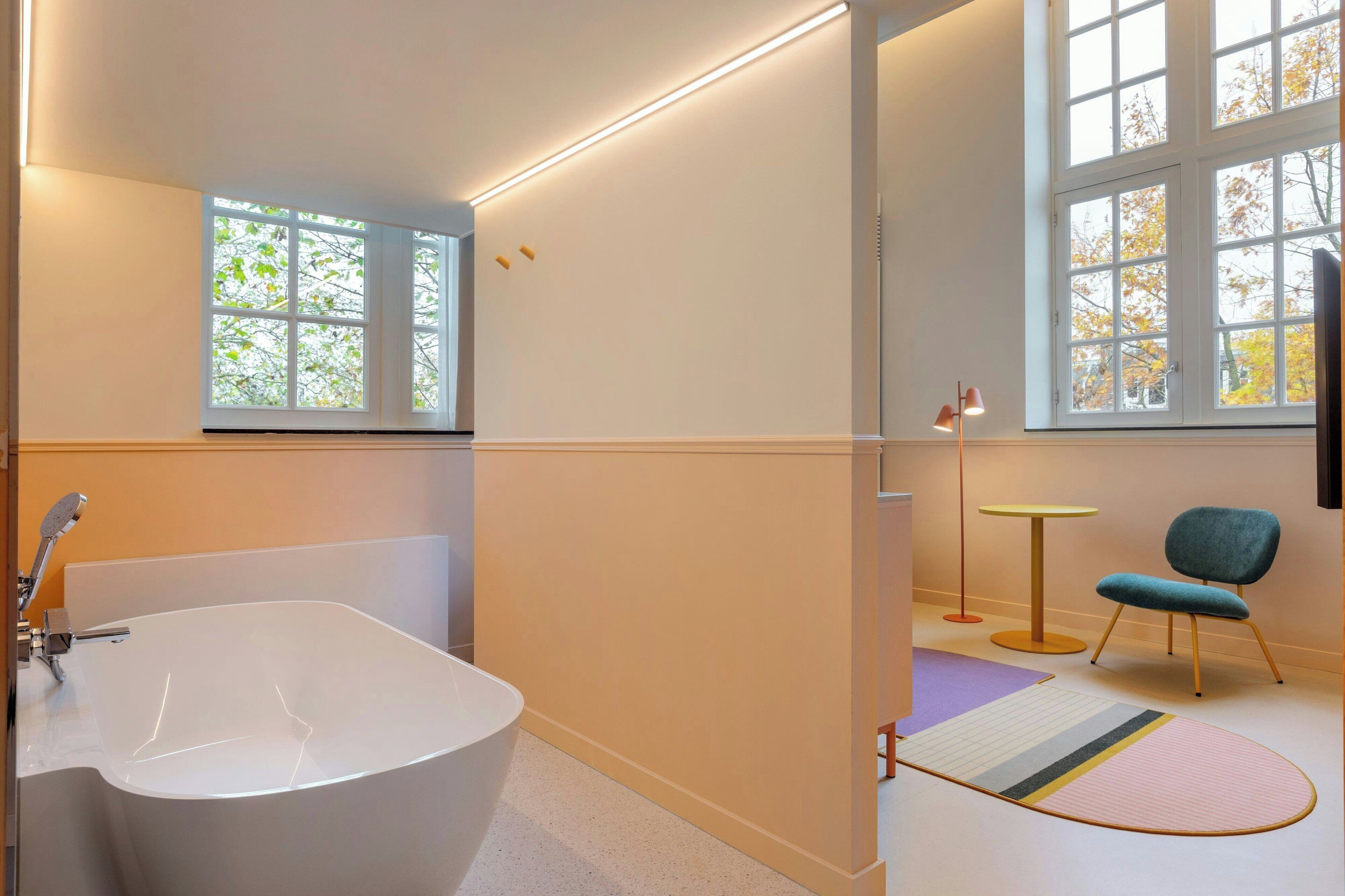 Un baño moderno con una bañera independiente, ventanas amplias y una pequeña mesa redonda con una silla.