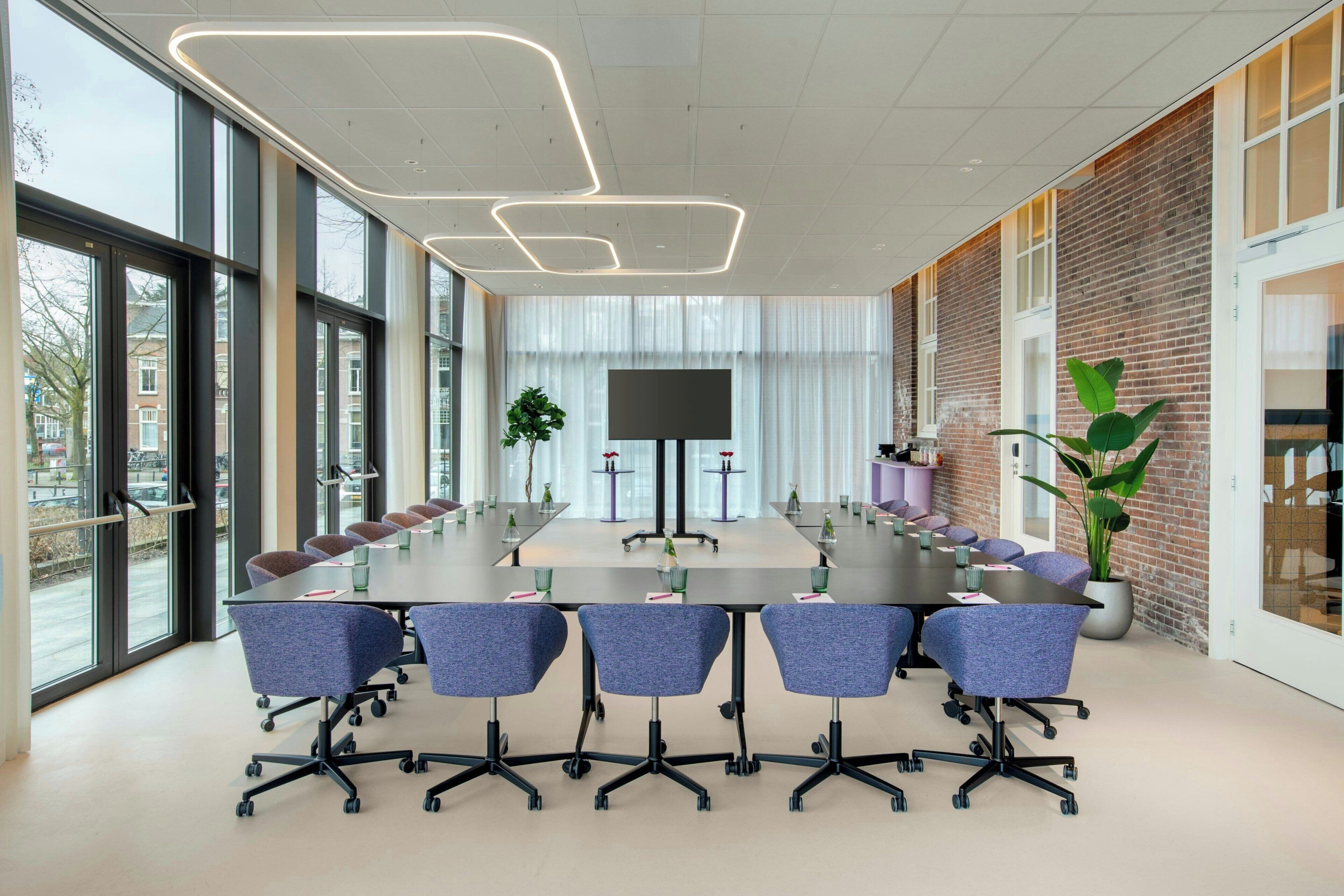 A conference room with a long table, chairs, a TV screen, and large windows.