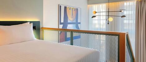 Habitación de hotel con cama, un cuadro en la pared, ventana con cortinas y una lámpara de techo original.