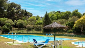 A swimming pool with blue and white lounge chairs, a thatched umbrella, and surrounding greenery.