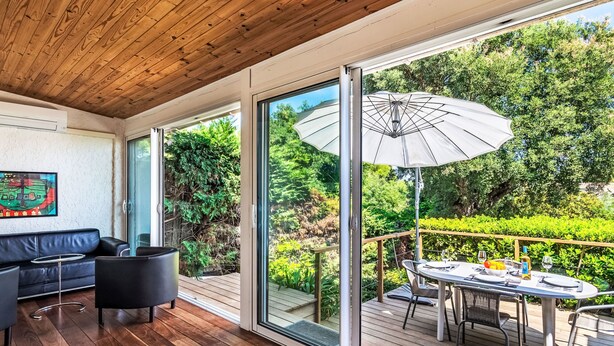 Una terraza moderna al aire libre con techo de madera, una mesa de comedor con sillas y un paraguas grande.