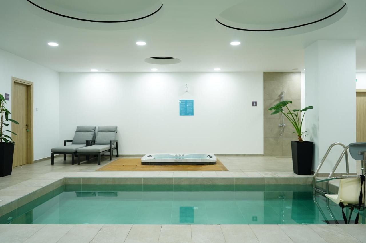A swimming pool with a hot tub, two lounge chairs, and potted plants.