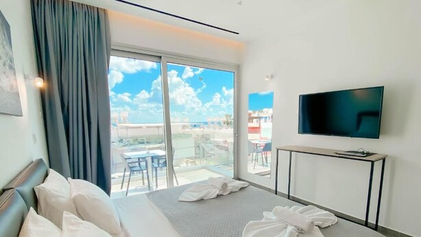 A hotel room with a bed, a TV, a balcony with a view, and a table. - Caramela Luxury Apartments (Ayia Napa)