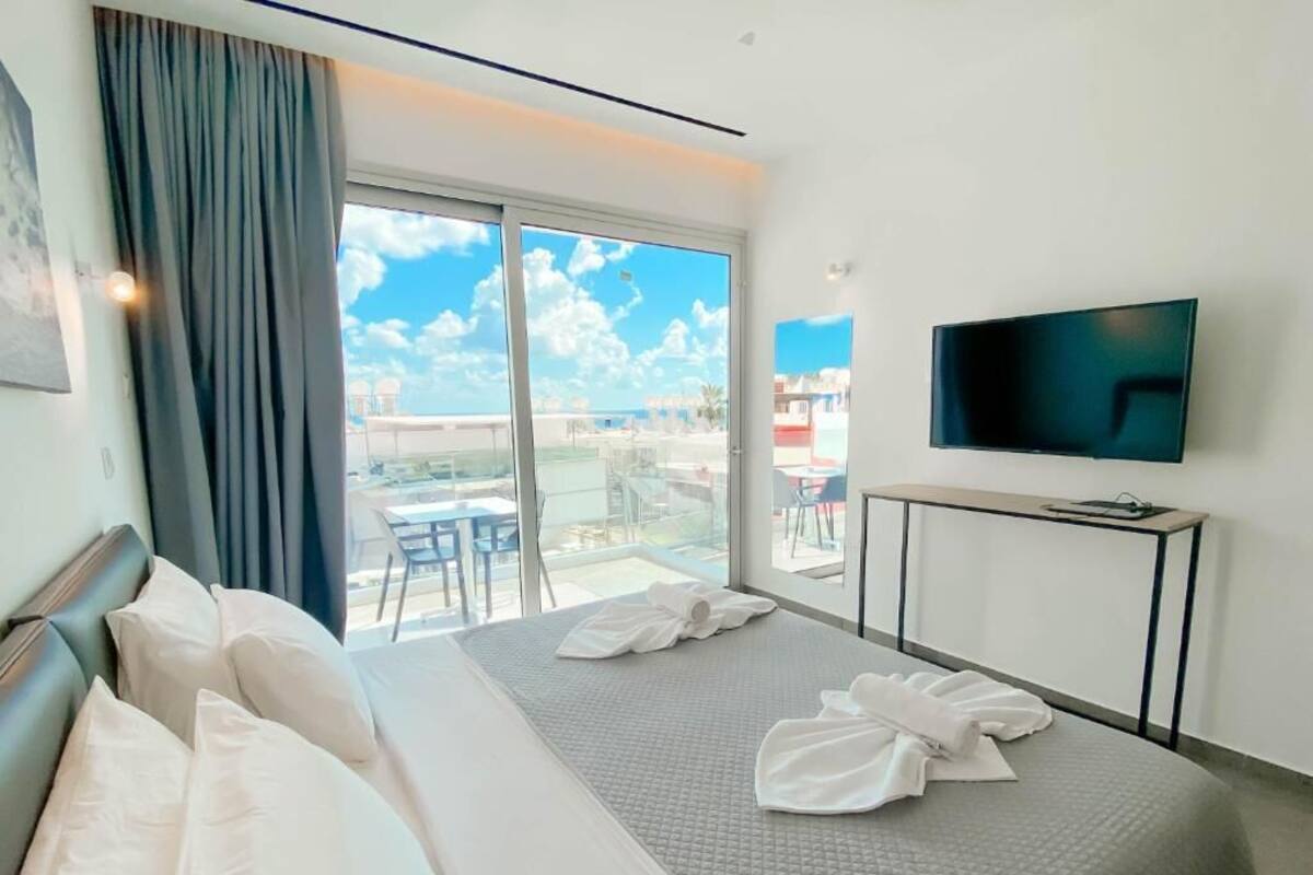 A hotel room with a bed, a TV, a balcony with a view, and a table.
