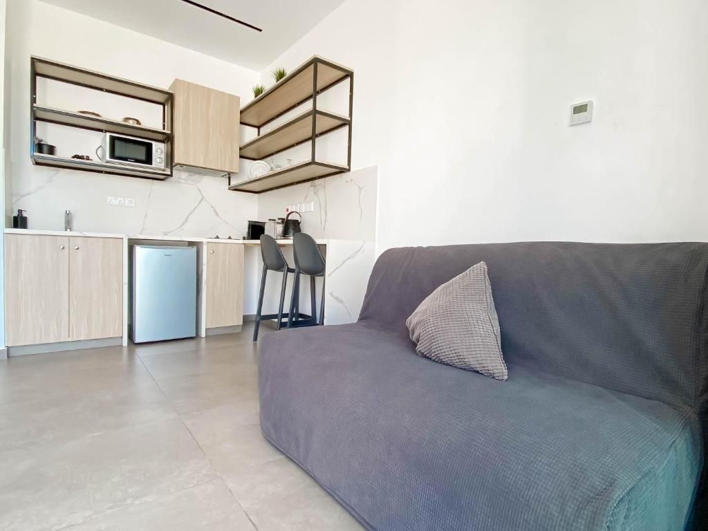 Una cocina moderna con microondas integrado, cafetera y refrigerador pequeño. En la sala de estar, hay un sofá gris con un cojín y una silla.