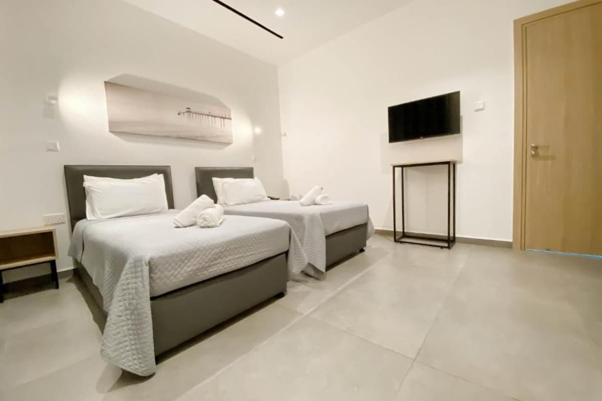A modern hotel room with two beds, a flat-screen TV, and a wooden door.