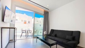 A modern living room with a black sofa, a glass table, and a view of the outside through a sliding glass door. - Caramela Luxury Apartments (Ayia Napa)