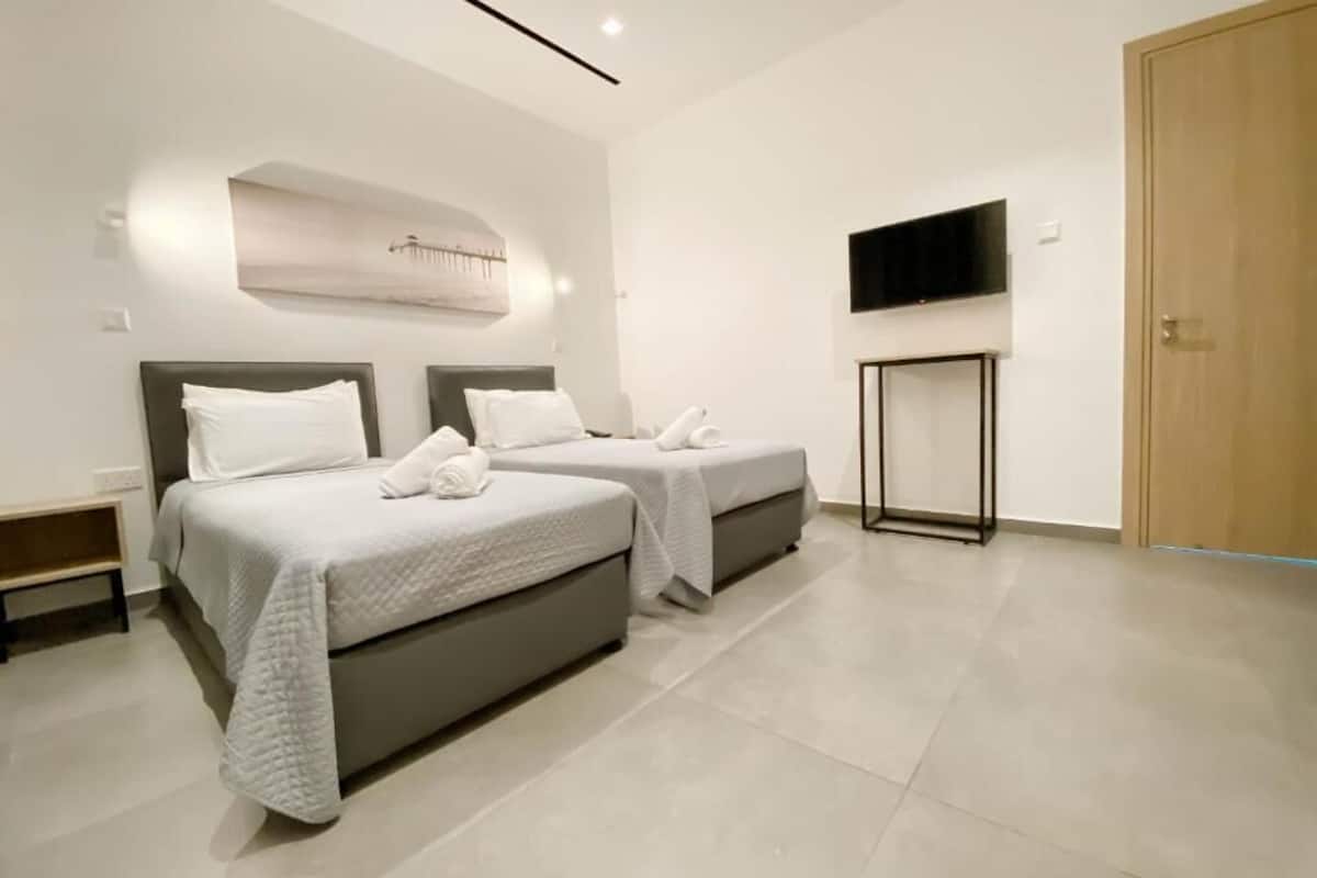 A modern hotel room with two beds, a flat-screen TV, and a wooden door.
