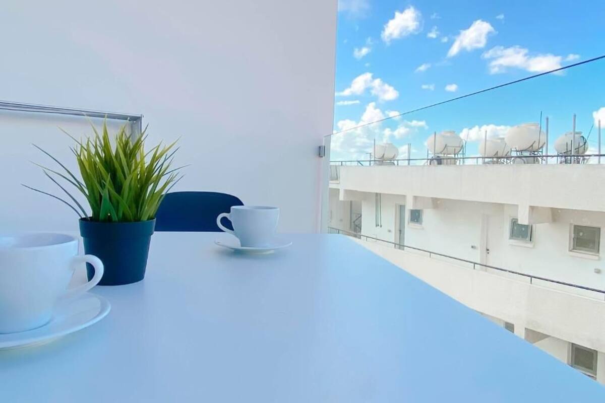 A balcony with a white table, two white cups, and a potted plant.